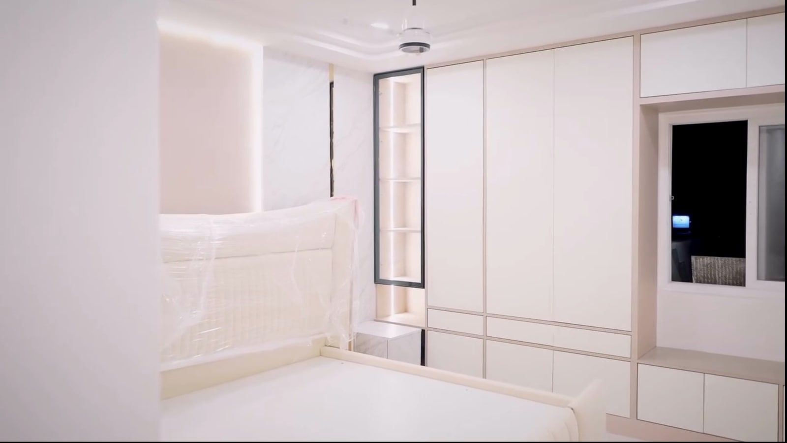 The same wall as built, the lit glass niche beside white shutters and the window seat, the bed still wrapped