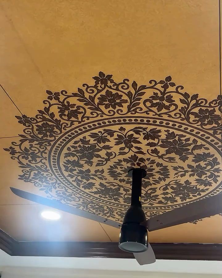 Stencilled dark floral mandala on an ochre ceiling, a fan at its centre