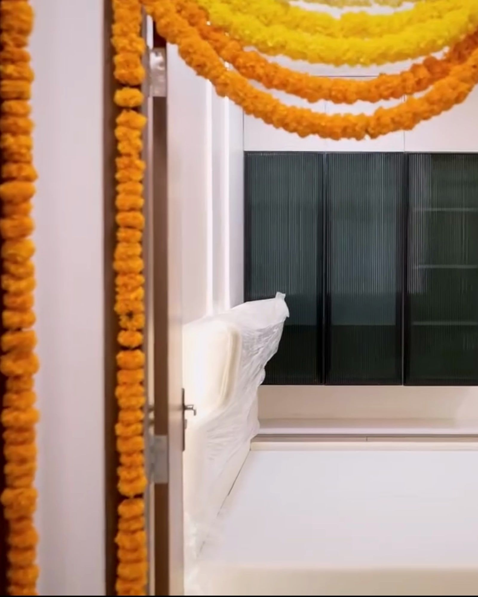 Bedroom doorway hung with marigold for the griha pravesam, tinted glass wardrobes beyond