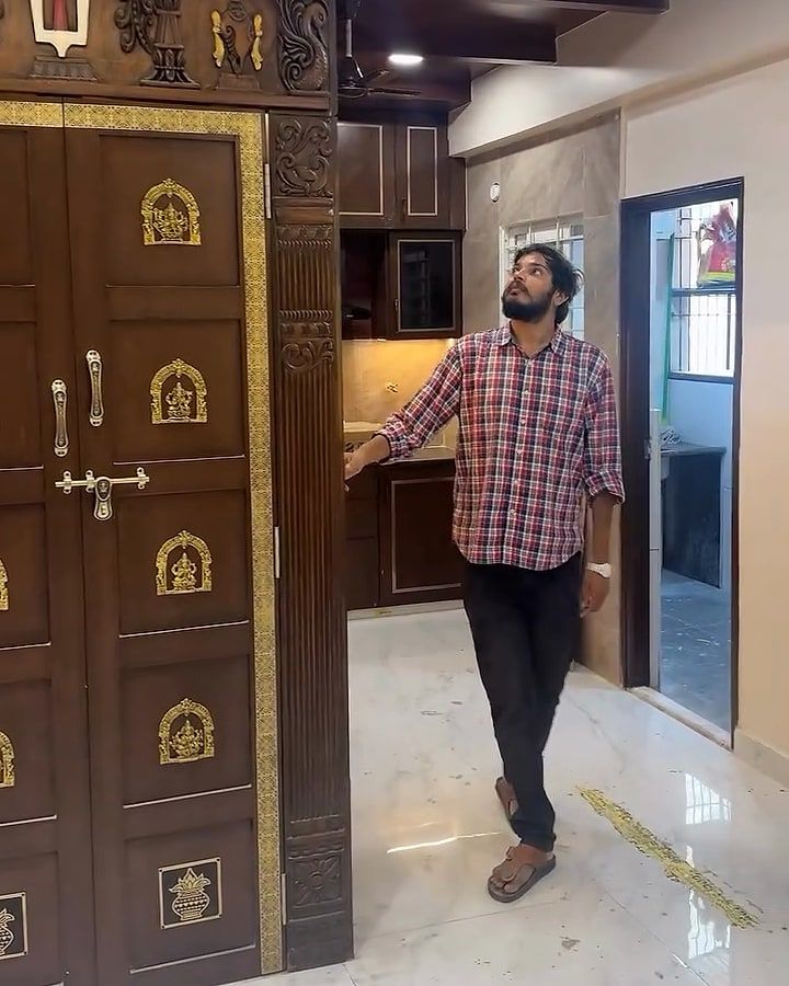 Panelled pooja doors with rows of brass deity plaques, a man looking up beside them